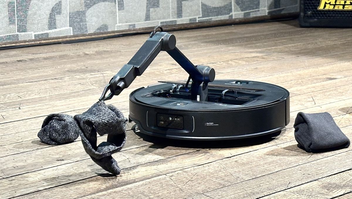 AI-powered robot vacuum with robotic arm picking up clothes from the floor — smart home cleaning innovation in action